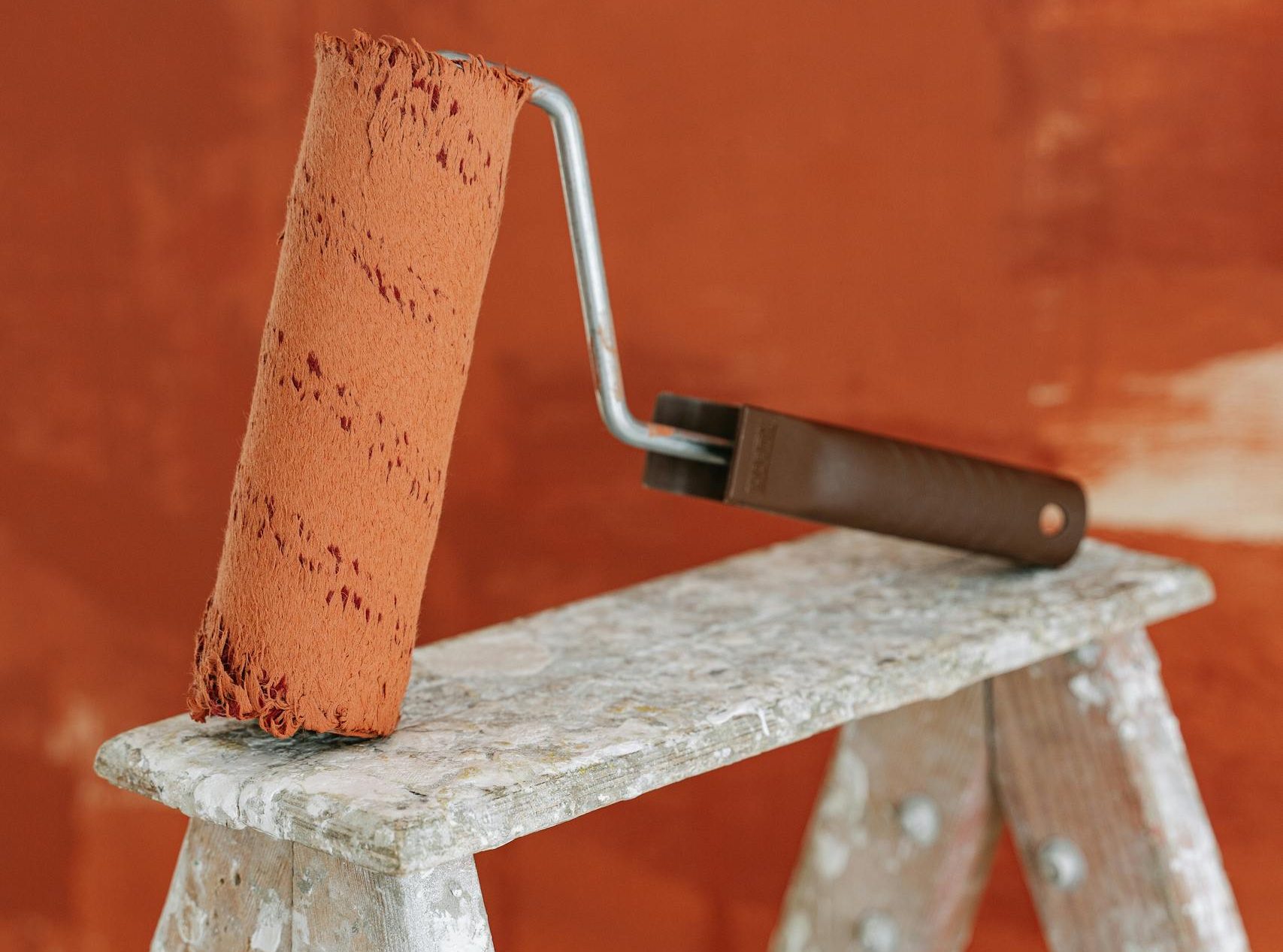 A paint roller rests on a stepladder against a painted wall, capturing a home renovation scene.